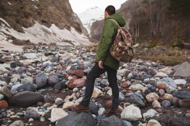 Genç hippi, nehir kenarında yürüyüş, vahşi doğa, kış tatili, seyahat, sırt çantası, sıcak kıyafetler, anorak, dağ manzarası, aktif.
