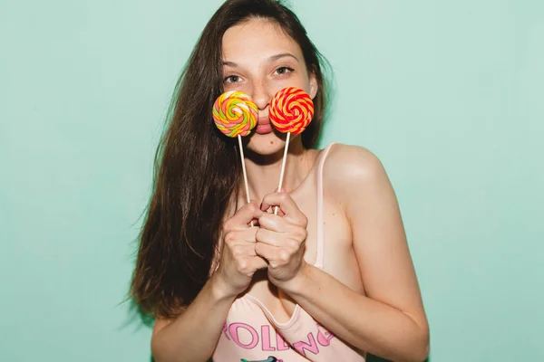 young beautiful hipster woman posing against blue wall, denim vintage style, pink swimsuit, blue jeans, holding eating lolly pop candy sexy