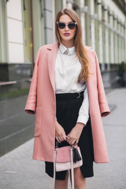 Oldukça çekici, güler yüzlü, zengin bir kadın pembe ceketli, bahar moda çantalı, zarif tarzda, güneş gözlüğü takıyor.