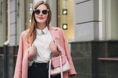 Çekici, şık, güler yüzlü, şehir caddesinde pembe ceketli, bahar moda çantalı, zarif tarzda, güneş gözlüğü takan bir kadın.