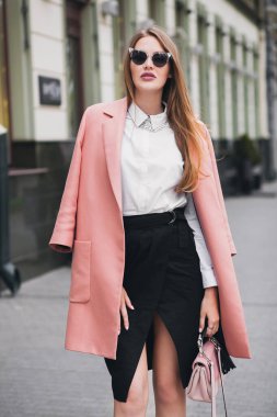 Havalı, genç, şık, güzel bir kadın sokakta yürüyor, pembe ceket, çanta, güneş gözlüğü, beyaz gömlek, siyah etek, moda kıyafeti, sonbahar modası, gülen mutlu aksesuarlar,