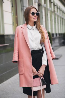 Çekici, şık, güler yüzlü, şehir caddesinde pembe ceketli, bahar moda çantalı, zarif tarzda, güneş gözlüğü takan bir kadın.