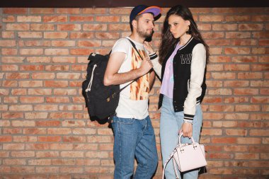 Genç, şık bir hippi çift, şık kıyafetler, kot pantolon, kucak, havalı aksesuarlar, tuğla duvara karşı poz, klasik tarz.