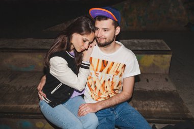 Genç şık hippi çift aşık, şık kıyafetler, kot pantolon, kucak, havalı aksesuarlar, mutlu mesut oturup, eğleniyorlar.
