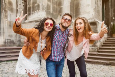 Genç hippi arkadaş grubu seyahat ediyor, klasik tarz, Avrupa tatili, güneş gözlüğü, eski şehir merkezi, mutlu ruh hali, gülümsüyor, kucaklıyor, işaret ediyor, ileriye bakıyor.