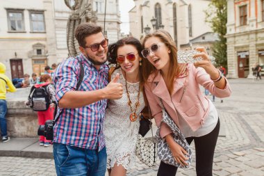 Genç hippi arkadaş grubu seyahat ediyor, klasik tarz, Avrupa tatili, güneş gözlüğü, eski şehir merkezi, mutlu bir ruh hali, gülümsüyor, kucaklıyor, akıllı telefondan selfie çekiyor.