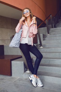 Avrupa 'da seyahat eden genç, güzel bir kadın, yaz tatili, güneş gözlükleri, pembe deri ceket, Glam Rock tarzı, şehir tarzı, alışveriş çantası.
