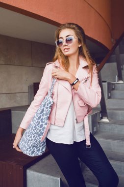 Avrupa 'da seyahat eden genç, güzel bir kadın, yaz tatili, güneş gözlükleri, pembe deri ceket, Glam Rock tarzı, şehir tarzı, alışveriş çantası.