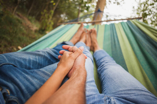 man and woman in love lying in hammock embracing, holding hands together, legs, close-up details, romance, autumn vacation, forest, relaxing, barefoot, jeans, denim outfit