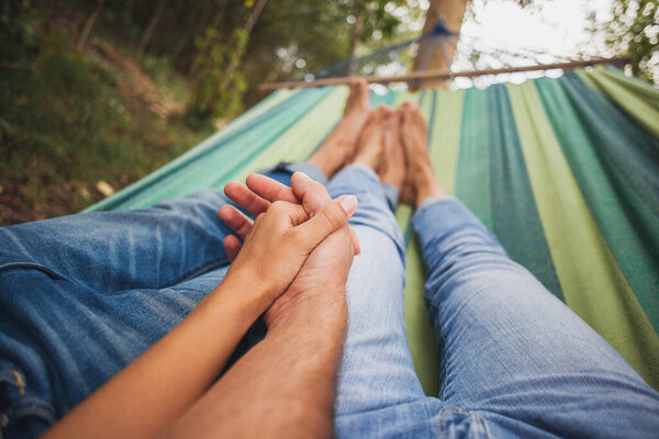 man and woman in love lying in hammock embracing, holding hands together, legs, close-up details, romance, autumn vacation, forest, relaxing, barefoot, jeans, denim outfit