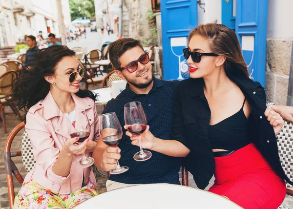 young hipster company of friends sitting in city street cafe, holding glasses, toasting, celebrating, drinking wine, sunglasses, summer vacation, party, having fun, smiling, happy, positive