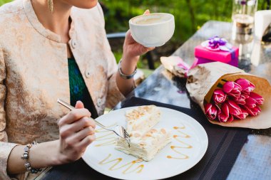 Kafede oturan, elinde bardak kapuçino tutan, lezzetli pastalar yiyen, laleler, doğum günü partisi, Avrupa tatili, detaylar, ellerinizi kapatın, romantik bir akşam yemeği.