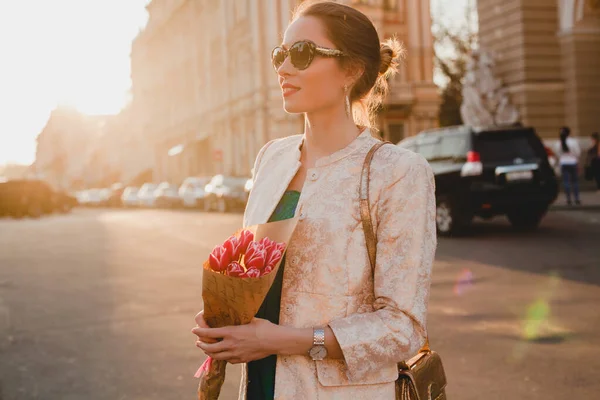 年轻而时尚的美女在日落时走在城市街道上 带着郁金香花束 太阳镜 时髦服装 — 图库照片
