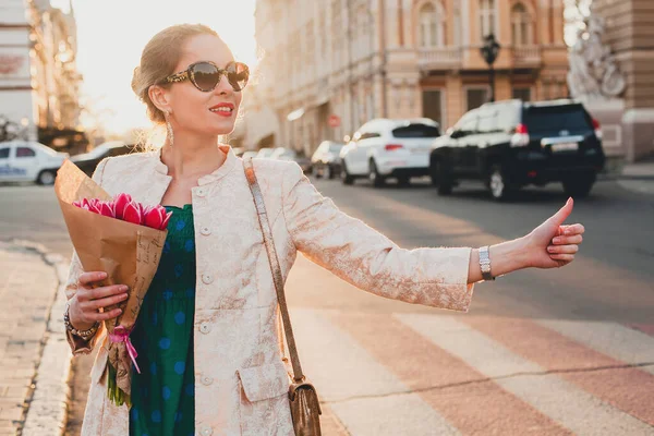 若いスタイリッシュな美しい女性は日没時に街を歩く タクシーを引く 手を振って ヨーロッパの休暇 チューリップの花束 春の傾向 サングラス ファッション衣装 ジャケットを保持 — ストック写真