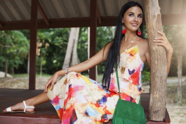 Renkli elbiseli genç seksi kadın, yaz hippi tarzı, tropik tatil, bronzlaşmış bacaklar, sandaletler, püsküllü yeşil çanta, aksesuarlar, gülümseyen, mutlu