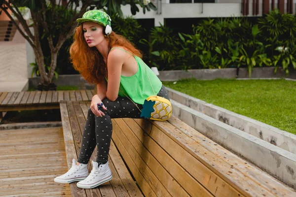 年轻时尚的时髦女人 坐在长椅上 听音乐 绿色帽子 太阳镜 运动鞋 有乐趣的时髦服装 青少年 时尚配件 — 图库照片
