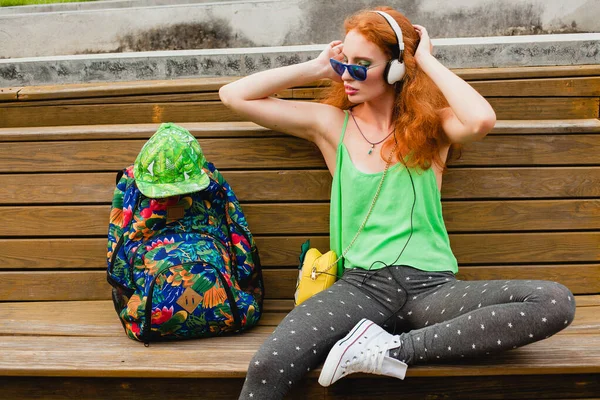 年轻时髦的嬉皮士生姜女士 坐在长椅上 听音乐 太阳镜 运动鞋 有乐趣的时髦服装 — 图库照片