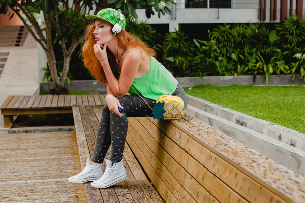 年轻时尚的时髦女人 坐在长椅上 听音乐 绿色帽子 太阳镜 有乐趣 时髦的服装 青少年 时尚配件 — 图库照片