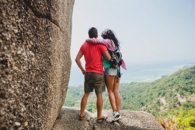 Genç ve mutlu bir hippi çift dünyayı geziyor, Tayland 'da romantik bir tatil, bir kayanın üzerinde oturuyor, parmakla işaret ediyor, aktif turizm, yaz tatili.