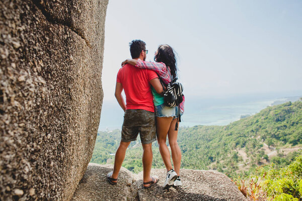 young happy hipster couple in love traveling around world, sightseeing, tropical romantic vacation in thailand, sitting on a rock, pointing finger, active tourism, summer