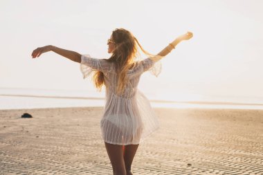 Genç, ince, güzel bir kadın gün batımı kumsalında, neşeli, dans, koşu, bohem kıyafeti, indie tarzı, yaz tatili, güneşli, eğleniyor, pozitif ruh hali, romantik, su sıçratan, siluet, mutlu.