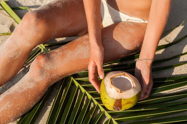 details of hands of sexy skinny woman in white bikini swimwear holding coconut drink, hips, sitting on tropical beach. slim body, sand on skin, vacation in Thailand, natural beauty, sunnyvsummer