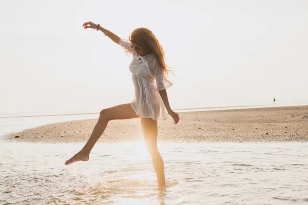 young slim beautiful woman on sunset beach, playful, dancing, running, bohemian outfit, indie style, summer vacation, sunny, having fun, positive mood, romantic, splashing water, silhouette, happy
