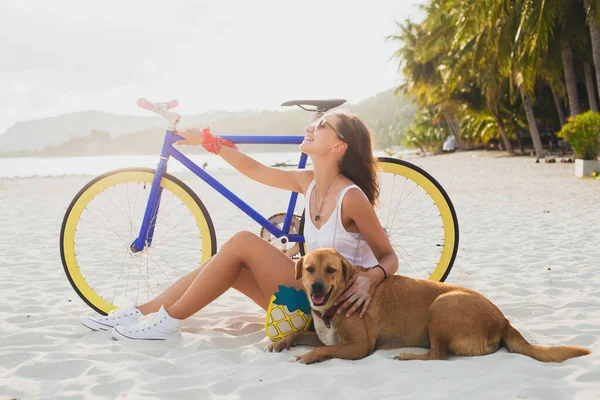 ビーチで砂の上に座っている若い美しい女性 ヴィンテージ自転車を保持 抱擁犬 幸せな気分 ヒップスターカジュアル衣装 サングラス スリムボディ 夏休み リラックス — ストック写真