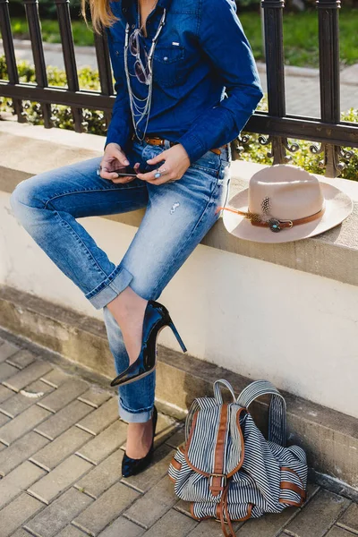 young stylish pretty woman, hands holding a phone, dressed in denim shirt and jeans, high heel shoes, hat, backpack, sunny day, good weather, city street, vacation europe, travel, detail, accessories