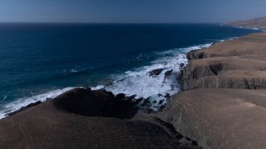  Kuvvetli dalgalarla kayalıklara çarpan kayalık kıyı şeridi berrak bir gökyüzü altında, derin mavi okyanus ve çorak kara arasındaki zıtlığı gözler önüne seriyor..
