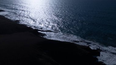  Kuvvetli dalgalarla kayalıklara çarpan kayalık kıyı şeridi berrak bir gökyüzü altında, derin mavi okyanus ve çorak kara arasındaki zıtlığı gözler önüne seriyor..