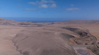 Görüntü, ıssız ve kurak bir arazinin havadan görünüşünü gösteriyor. Olay yerinden geçen toprak bir yol baraja ve neredeyse kurumuş bir su deposuna çıkıyor. Çevredeki arazi kuru olarak karakterize edilir., 