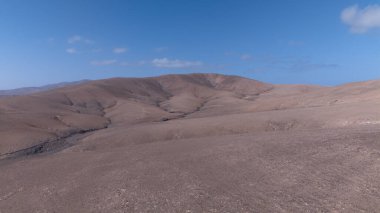Görüntü, ıssız ve kurak bir arazinin havadan görünüşünü gösteriyor. Olay yerinden geçen toprak bir yol baraja ve neredeyse kurumuş bir su deposuna çıkıyor. Çevredeki arazi kuru olarak karakterize edilir., 