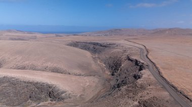 Görüntü, ıssız ve kurak bir arazinin havadan görünüşünü gösteriyor. Olay yerinden geçen toprak bir yol baraja ve neredeyse kurumuş bir su deposuna çıkıyor. Çevredeki arazi kuru olarak karakterize edilir., 