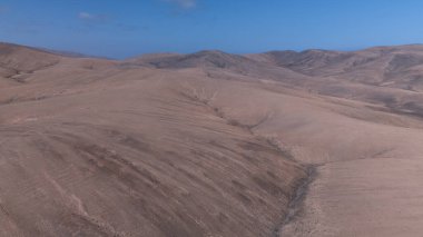 Yuvarlanan kahverengi tepeleri ufka kadar uzanan engin kurak bir manzara. Derin mavi okyanus berrak, parlak bir gökyüzünün altında zıt düşerken bir kanyon kuru araziyi kesiyor..