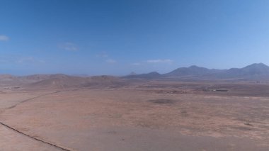 Yuvarlanan kahverengi tepeleri ufka kadar uzanan engin kurak bir manzara. Derin mavi okyanus berrak, parlak bir gökyüzünün altında zıt düşerken bir kanyon kuru araziyi kesiyor..