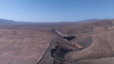 Uçsuz bucaksız, dolambaçlı bir yol, kuru tepeler ve berrak mavi gökyüzünün altındaki uzak dağlar tarafından çerçevelenmiş neredeyse boş bir rezervuar..