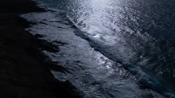  Kuvvetli dalgalarla kayalıklara çarpan kayalık kıyı şeridi berrak bir gökyüzü altında, derin mavi okyanus ve çorak kara arasındaki zıtlığı gözler önüne seriyor..