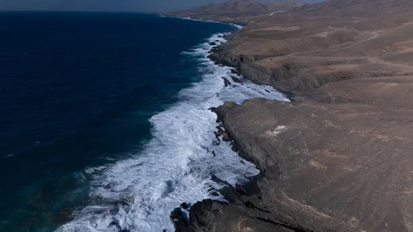  Kuvvetli dalgalarla kayalıklara çarpan kayalık kıyı şeridi berrak bir gökyüzü altında, derin mavi okyanus ve çorak kara arasındaki zıtlığı gözler önüne seriyor..