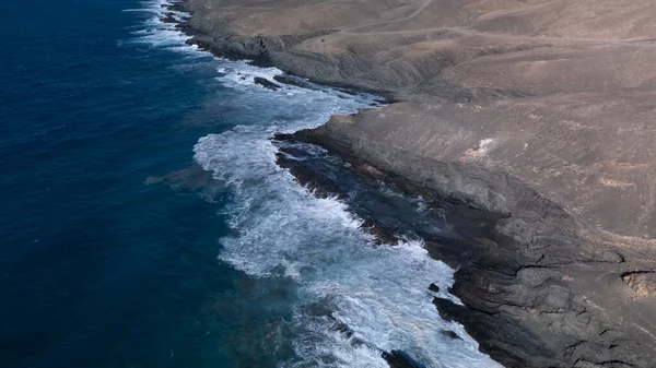  Kuvvetli dalgalarla kayalıklara çarpan kayalık kıyı şeridi berrak bir gökyüzü altında, derin mavi okyanus ve çorak kara arasındaki zıtlığı gözler önüne seriyor..