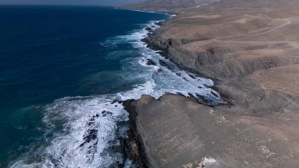  Kuvvetli dalgalarla kayalıklara çarpan kayalık kıyı şeridi berrak bir gökyüzü altında, derin mavi okyanus ve çorak kara arasındaki zıtlığı gözler önüne seriyor..