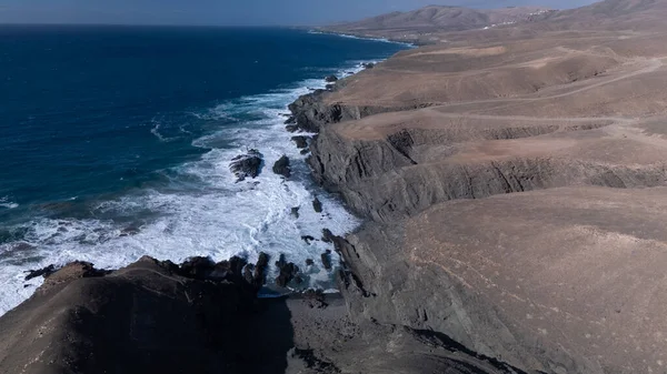  Kuvvetli dalgalarla kayalıklara çarpan kayalık kıyı şeridi berrak bir gökyüzü altında, derin mavi okyanus ve çorak kara arasındaki zıtlığı gözler önüne seriyor..