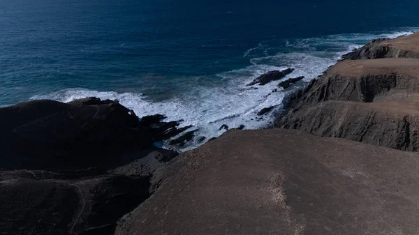  Kuvvetli dalgalarla kayalıklara çarpan kayalık kıyı şeridi berrak bir gökyüzü altında, derin mavi okyanus ve çorak kara arasındaki zıtlığı gözler önüne seriyor..