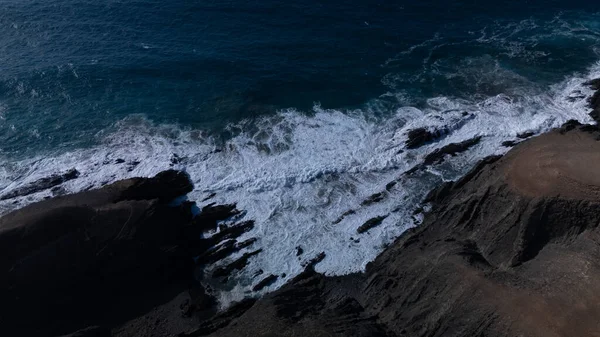  Kuvvetli dalgalarla kayalıklara çarpan kayalık kıyı şeridi berrak bir gökyüzü altında, derin mavi okyanus ve çorak kara arasındaki zıtlığı gözler önüne seriyor..