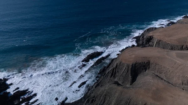  Kuvvetli dalgalarla kayalıklara çarpan kayalık kıyı şeridi berrak bir gökyüzü altında, derin mavi okyanus ve çorak kara arasındaki zıtlığı gözler önüne seriyor..