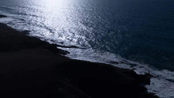 Kuvvetli dalgalarla kayalıklara çarpan kayalık kıyı şeridi berrak bir gökyüzü altında, derin mavi okyanus ve çorak kara arasındaki zıtlığı gözler önüne seriyor..