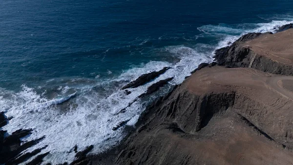  Kuvvetli dalgalarla kayalıklara çarpan kayalık kıyı şeridi berrak bir gökyüzü altında, derin mavi okyanus ve çorak kara arasındaki zıtlığı gözler önüne seriyor..