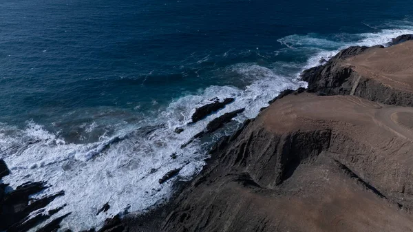  Kuvvetli dalgalarla kayalıklara çarpan kayalık kıyı şeridi berrak bir gökyüzü altında, derin mavi okyanus ve çorak kara arasındaki zıtlığı gözler önüne seriyor..