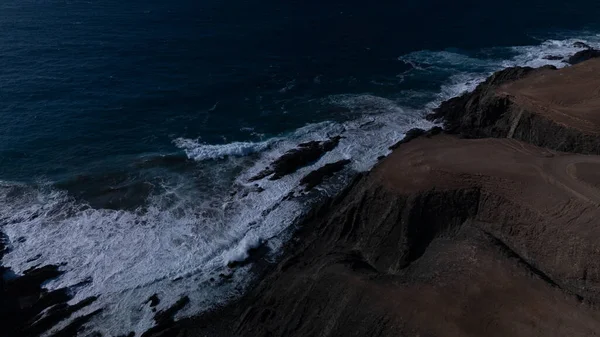  Kuvvetli dalgalarla kayalıklara çarpan kayalık kıyı şeridi berrak bir gökyüzü altında, derin mavi okyanus ve çorak kara arasındaki zıtlığı gözler önüne seriyor..