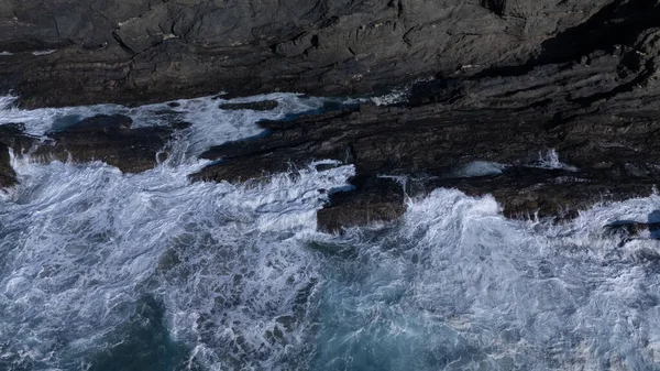 Kuvvetli dalgalarla kayalıklara çarpan kayalık kıyı şeridi berrak bir gökyüzü altında, derin mavi okyanus ve çorak kara arasındaki zıtlığı gözler önüne seriyor..